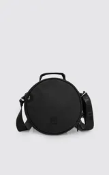 Bolso circular de estructura rígida, color negro, diseñado para el transporte de auriculares y accesorios. Cuenta con manija superior reforzada, correa de hombro ajustable con logo grabado, cierre perimetral y bolsillo trasero de acceso rápido.
