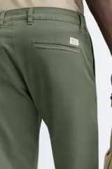 Pantalón chino de corte ajustado, color beige, con bolsillos laterales y bolsillos traseros de vivo. Cuenta con cierre frontal de cremallera y botón.