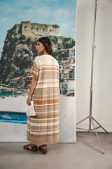 Vestido largo de tejido calado con rayas horizontales en tonos beige, marrón y amarillo. Tiene corte recto, hombros caídos, tajo lateral y logo bordado en la manga.