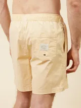 Short de baño tipo volley color amarillo claro, con cintura elástica y cordón ajustable. Presenta un diseño liso con un pequeño logo bordado en la parte inferior de la pierna izquierda.