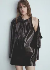 Vestido corto de efecto piel con diseño recto y cuello redondo. Presenta un corte sin mangas y cierre de cremallera invisible en la parte posterior.
