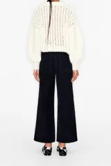 Pantalón culotte de pana color negro, tiro alto, largo tobillero, con cierre de cremallera y botón metálico, bolsillos traseros y trabillas para cinturón.