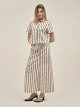 Falda larga color crudo con rayas verticales negras, corte recto, tajo frontal, cintura con cordón ajustable y bolsillos laterales.