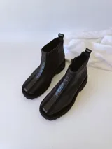 Botas negras de cuero con caña baja, cierre lateral con cremallera y suela track.