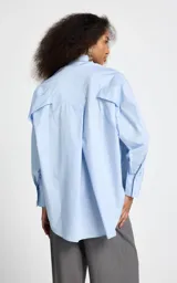 Camisa de corte oversize color celeste, con cuello clásico, cierre frontal de botones y mangas largas con puños abotonados.