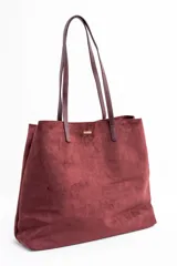 Bolso tipo tote de gran tamaño en color bordó, confeccionado en material con textura similar a la gamuza. Cuenta con doble asa larga para llevar al hombro y una pequeña placa metálica decorativa en el frente.