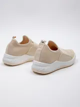 Zapatilla beige de tela tejida, con piezas de goma en los laterales y pieza elástica sobre el empeine. Plataforma texturada de 4 cm de alto.