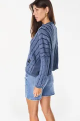 Sweater crop de tejido de punto con diseño trenzado y rayas verticales en combinación de tonos beige y tostado, cuello redondo y mangas murciélago largas. Cuenta con un parche de cuerina marrón con la marca grabada en el borde inferior.
