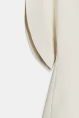 Top color crema de cuello redondo y manga corta abullonada. Presenta un bajo asimétrico y cierre en la espalda con cremallera oculta en la costura.