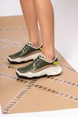 Championes urbanos de cuero verde con textura reptil, detalles en beige y amarillo, cordones negros y suela chunky blanca con base negra.