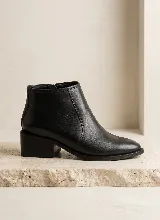 Bota corta de cuero vacuno color negro, con taco cuadrado de 5 cm y cierre lateral. Diseño minimalista con costuras visibles y suela de caucho antideslizante.
