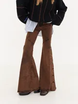 Jean de corte oxford con tiro medio, confeccionado en denim negro. Presenta recortes curvos en las piernas y detalle de botones metálicos en los laterales de la botamanga.