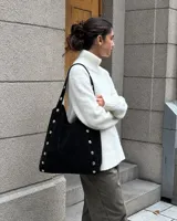 Cartera tipo tote de símil gamuza color negro, con diseño amplio y detalle de tachas metálicas en las costuras y las asas de hombro.