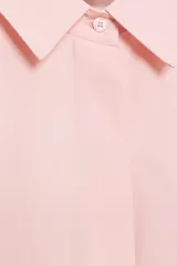 Camisa rosada de cuello solapa y manga larga, con detalle de volantes en las sisas y cierre frontal oculto con botones.