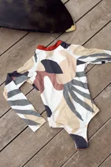 Enteriza de surf de mangas largas con espalda abierta y cuello redondo. Diseño estampado con formas abstractas en tonos beige, marrón, gris y negro.
