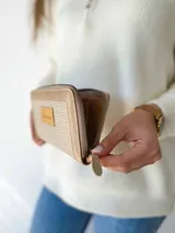 Billetera grande con cierre metálico, color beige. Presenta un panel central con textura tejida o tramada en tono claro y bordes de cuero liso en tono beige más oscuro. Posee un parche de cuero con la palabra "chouie" escrita a mano.