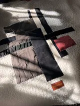 Campera de corderito blanco con diseño de collage geométrico en el frente, compuesto por parches de diferentes telas en tonos gris, negro, beige y un detalle en rojo. Incluye una etiqueta de cuero sintético con la marca The Mood.