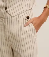 Pantalón recto de cintura alta, color beige con rayas verticales oscuras, bolsillos funcionales y detalle de aletas con botones en la cintura.