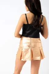 Short pollera de tiro bajo, confeccionado en tejido metalizado color dorado con acabado brillante y diseño plisado en la parte frontal.