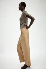 Pantalón de sarga en color beige, con tiro medio, cintura con trabillas y pernera recta. Presenta bolsillos de vivo en el delantero, cierre frontal con cremallera y botón metálico.