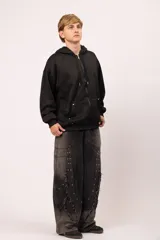 Campera oversize con capucha y cierre frontal metálico. Presenta bolsillos frontales con remaches metálicos y un diseño exclusivo en la espalda con la palabra "TACHA" formada por alfileres de gancho plateados. Confeccionada en tejido de jersey con interior suave.