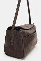 Mini bolso de mano confeccionado en piel, con asa corta, cierre de cremallera y solapa superior. Cuenta con bolsillos exteriores en la parte delantera y trasera, y un bolsillo interior con cierre.