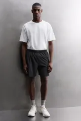 Pantalones cortos negros de tejido técnico perforado, ligeros y elásticos. Cuentan con cintura elástica ajustable con cordón interior, bolsillos frontales, bolsillo trasero de seguridad con cierre de cremallera, perneras con laterales perforados para transpirabilidad, bajo con acabado termofijado y aberturas laterales. Incluye detalle de logo estampado en la pernera.