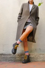 Bota tipo borcego de cuero en tono marrón con efecto desgastado, cordones bicolores en amarillo y naranja, y suela de goma dentada con costura blanca visible.