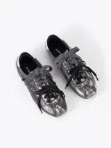 Zapatilla de cuero vacuno en tono gris oscuro metalizado, con detalles en cuero descarne. Presenta doble cordón, uno de ellos tejido, y charms decorativos. Cuenta con un detalle en color plateado en el talón y suela de goma en tono claro.