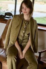 Chaleco de textura aterciopelada en tono marrón, con solapas amplias y diseño estructurado. Se combina con una blusa a tono que presenta detalle de volados frontales.