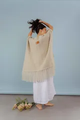 Ruana beige de lana merino tejida a mano, con diseño abierto, textura de punto y flecos en el borde inferior.