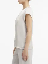 Blusa de satén color gris claro, con cuello redondo y abertura en forma de gota. Tiene mangas cortas con costuras en los hombros y cierre con broche en la espalda.