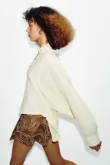 Camisa de cuello solapa y manga larga con sisa ancha, confeccionada en tejido con hilo metalizado y cierre frontal con botones.
