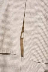Trench corto de corte oversize con estampado de cuadros finos en tonos beige y verde. Presenta cuello camisero en contraste de color marrón oscuro, cierre frontal con botones y mangas largas con detalle de trabas en los puños.