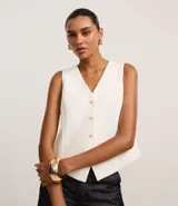 Chaleco sastre color blanco hueso, con escote en V y cierre frontal de tres botones dorados. Corte entallado con tajos laterales en el ruedo inferior.