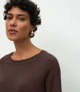 Suéter de punto color marrón chocolate, con cuello redondo y mangas largas con puños acanalados. Presenta un diseño básico y versátil de corte recto.