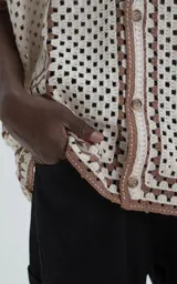 Camisa de manga corta tejida en punto abierto (símil crochet), color beige con detalles en marrón. Presenta cuello solapa, cierre frontal con botones y calce oversize.