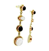 Aretes largos colgantes, con engarces de bronce, compuestos por cuatro elementos: un cabezal redondo con piedra negra, un óvalo con piedra blanca nacarada, un círculo con piedra negra y un colgante inferior redondo con piedra blanca nacarada.