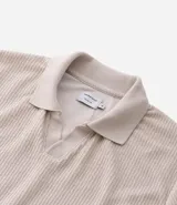Polo de manga larga color beige claro, confeccionado en tejido texturizado (posiblemente acanalado o waffle). Presenta un cuello polo con escote profundo en V sin botones.