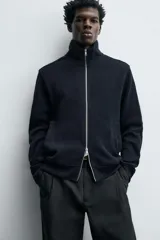 Chaqueta regular fit de cuello subido, confeccionada en tejido técnico interlock de algodón con elasticidad. Presenta cierre frontal con cremallera, manga larga con puños en rib y bolsillos de vivo en la cadera.