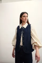 Chaleco azul de denim con cuello en V y cierre frontal con botones metálicos. Posee bolsillos delanteros y corte clásico.