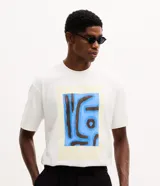 Remera de corte boxy confeccionada en algodón, con cuello redondo y manga corta. Presenta una estampa frontal con diseño artístico abstracto en tonos azules y marrones sobre un fondo claro.