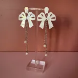 Par de aros colgantes con forma de lazo blanco, cadena plateada y perlas.