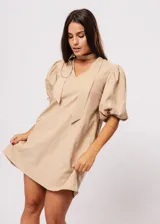 Vestido corto color beige, de corte oversize, con escote en V y mangas globo. Incluye cinturón marrón con hebilla dorada.