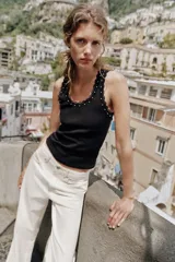 Musculosa de algodón color negro, con escote redondo y tiras anchas. Presenta detalles de encaje negro en los bordes y aplicación de perlas pequeñas alrededor del escote y los hombros.
