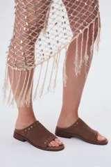 Sandalias bajas de cuero color marrón con detalles de tachas metálicas.