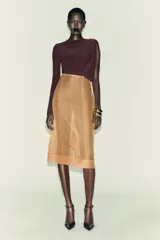 Body de manga larga color marrón oscuro, con escote asimétrico drapeado y detalle de broche metálico en el hombro derecho.