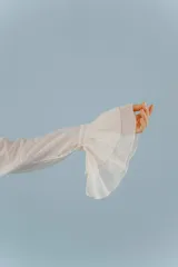 Camisa de estilo romántico confeccionada en algodón, con cuello alto, volados frontales y mangas largas con puños acampanados también decorados con volados.