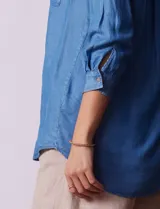 Blusa celeste de lyocell con cuello con solapa, escote en V y cierre con botones. Tiene un bolsillo en el pecho, mangas 3/4 con puño y botón.