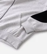 Buzo con capucha y cierre frontal, confeccionado en tejido fleece de algodón y poliéster. Presenta un diseño bicolor con cuerpo en gris melange y paneles laterales en las mangas de color negro, bolsillos frontales, y puños y ruedo en rib.